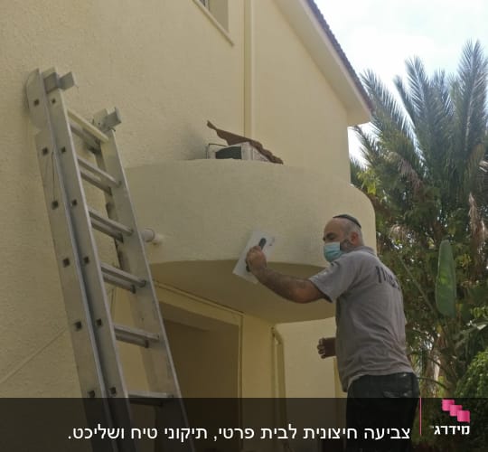 אדם עם מסכה צובע קיר חיצוני בעזרת שפכטל